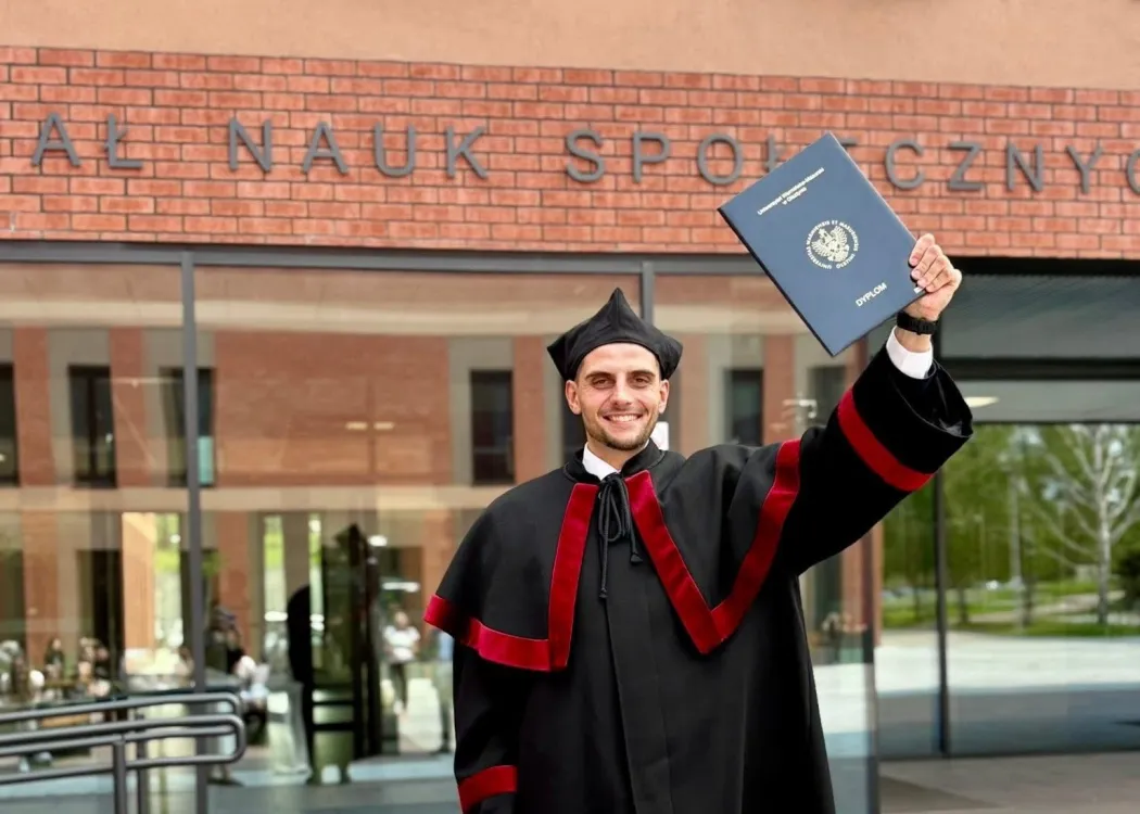 Jakub Klepański pozuje z pracą doktorską przed Wydziałem Nauk Społecznych 
