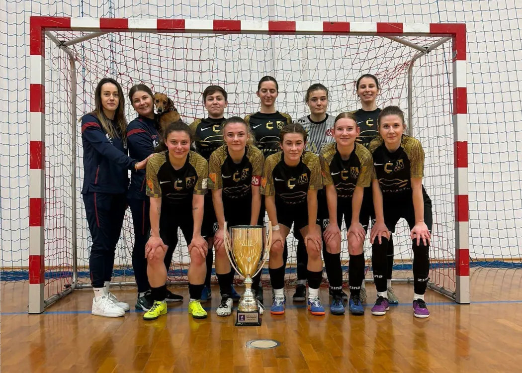 Drużyna AZS UWM High Heels pozuje do zdjęcia z pucharem na tle bramki 