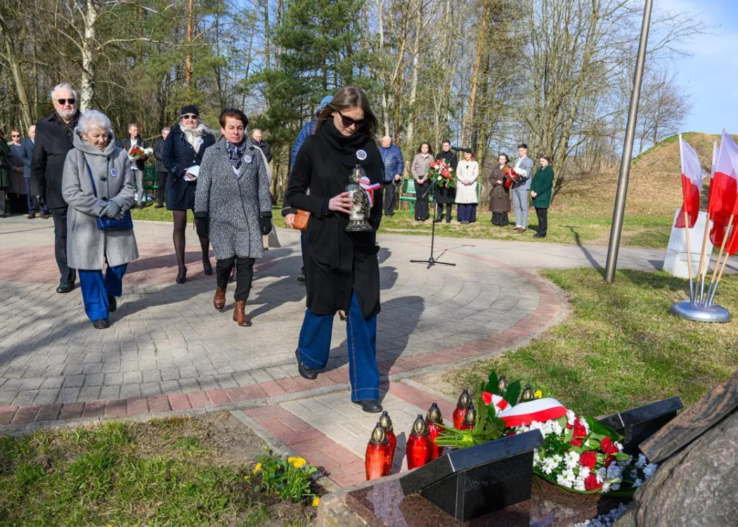 Uczestnicy uroczystości upamiętniającej ofiary zbrodni katyńskiej składają kwiaty pod tablicą pamiątkową.