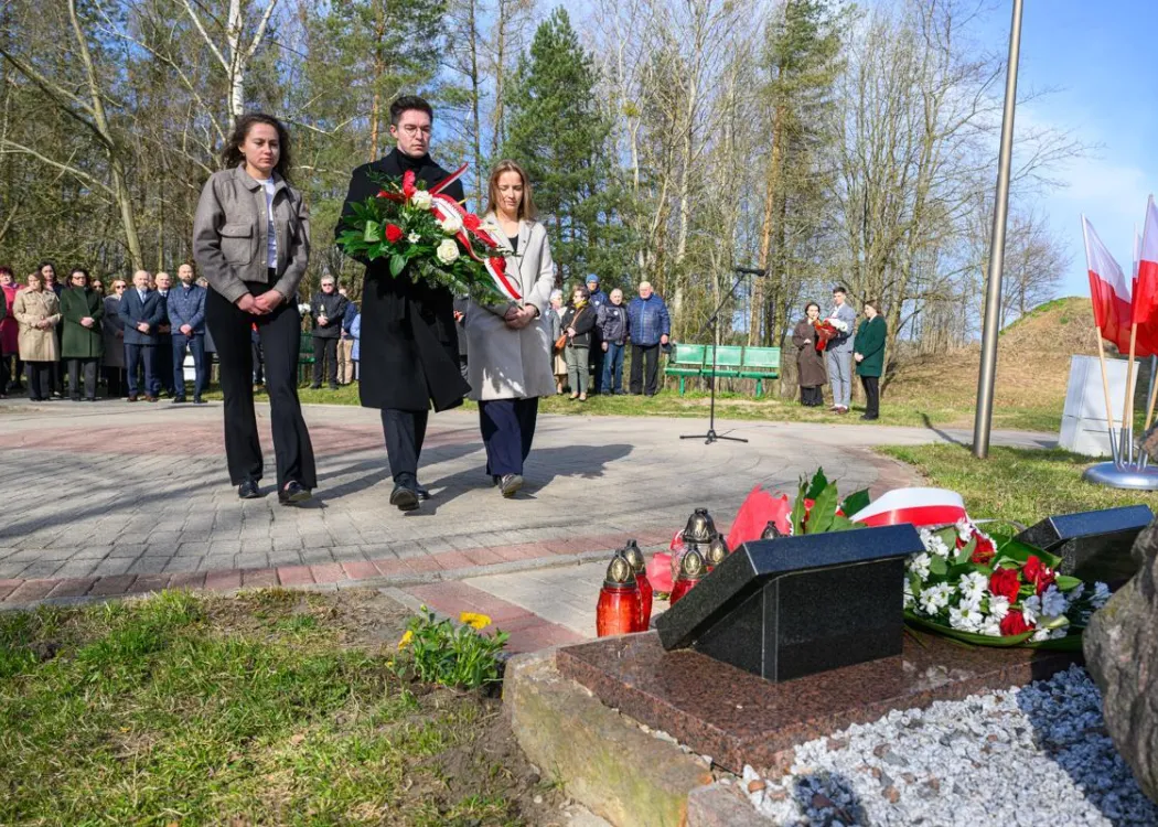 Uczestnicy uroczystości upamiętniającej ofiary zbrodni katyńskiej składają kwiaty pod tablicą pamiątkową.