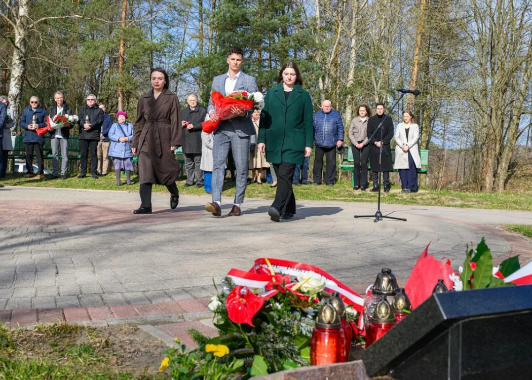 Uczestnicy uroczystości upamiętniającej ofiary zbrodni katyńskiej składają kwiaty pod tablicą pamiątkową.