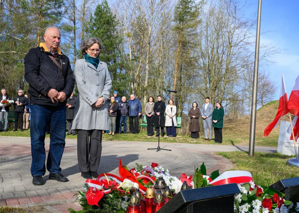 Uczestnicy uroczystości upamiętniającej ofiary zbrodni katyńskiej składają kwiaty pod tablicą pamiątkową.