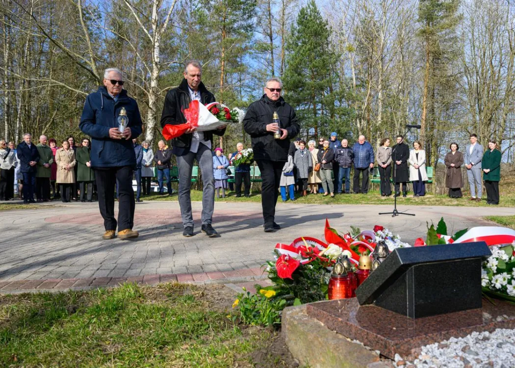 Uczestnicy uroczystości upamiętniającej ofiary zbrodni katyńskiej składają kwiaty pod tablicą pamiątkową.