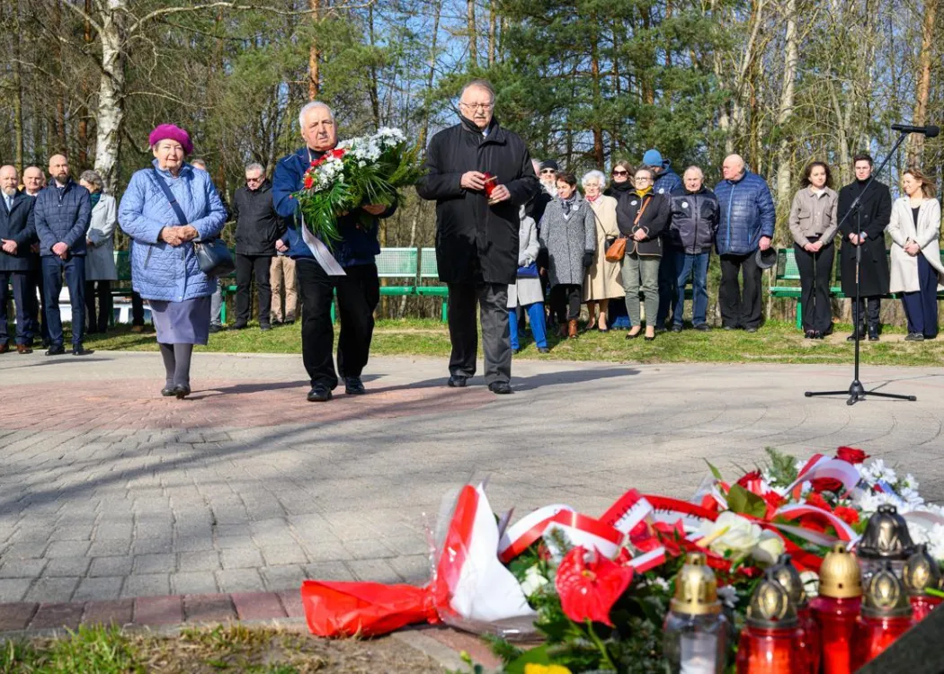Uczestnicy uroczystości upamiętniającej ofiary zbrodni katyńskiej składają kwiaty pod tablicą pamiątkową.