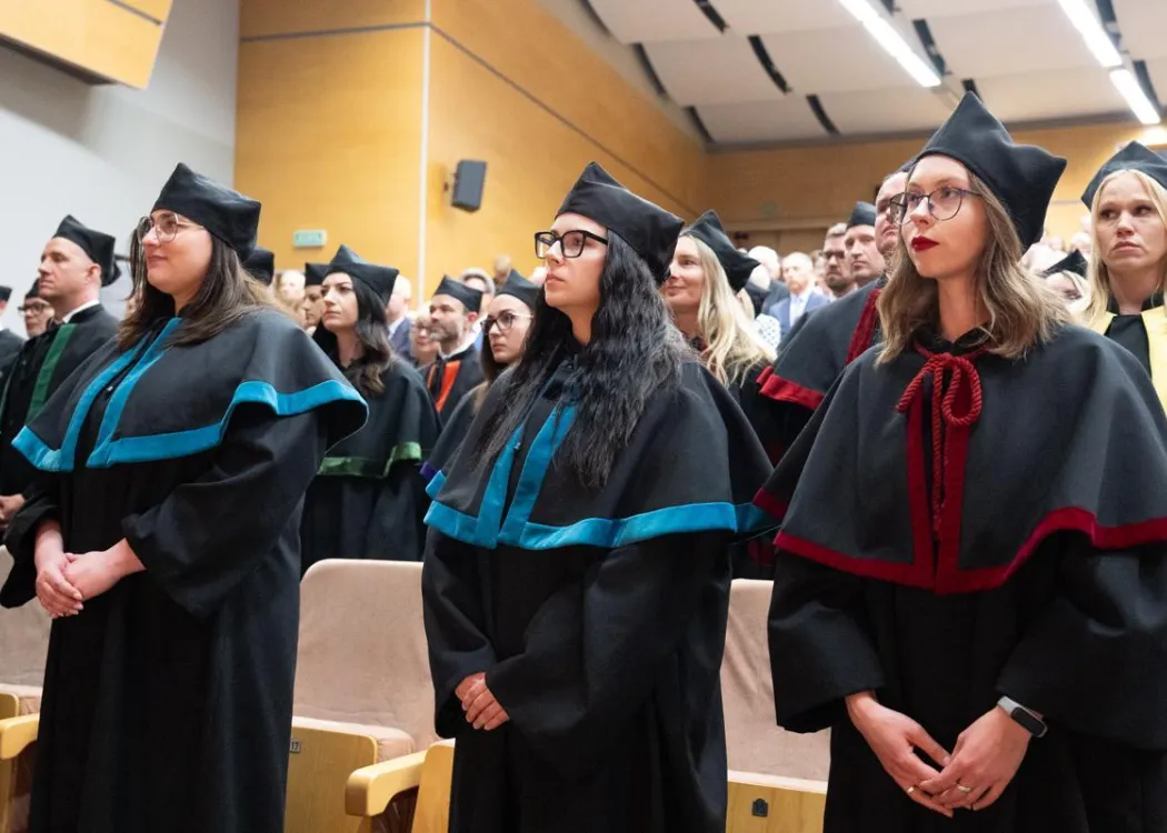 Święto Uniwersytetu 2026: wypromowani doktorzy i doktorzy habilitowani stoją na widowni podczas uroczystości