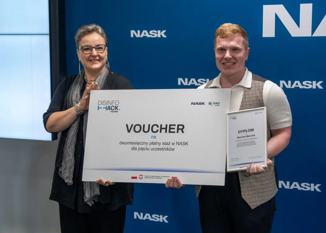 Marcin Merchel odbiera voucher od przedstawicielki organizatorów konkursu DISINFOHACK 2026