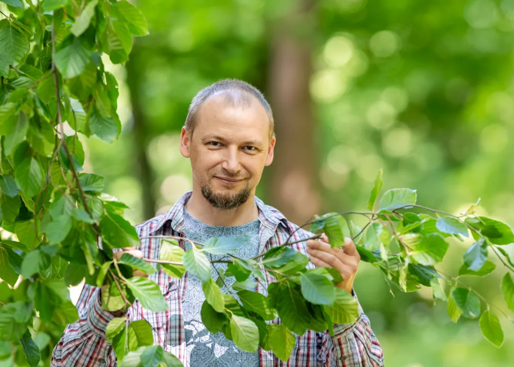 Marcin Michalak stoi przy drzewach i trzyma gałązkę 