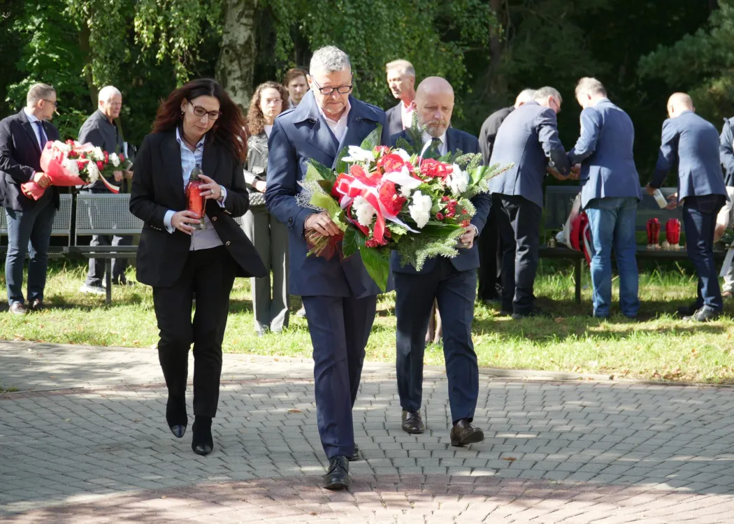 Troje przedstawicieli kolegium rektorskiego UWM niosą kwiaty i znicze
