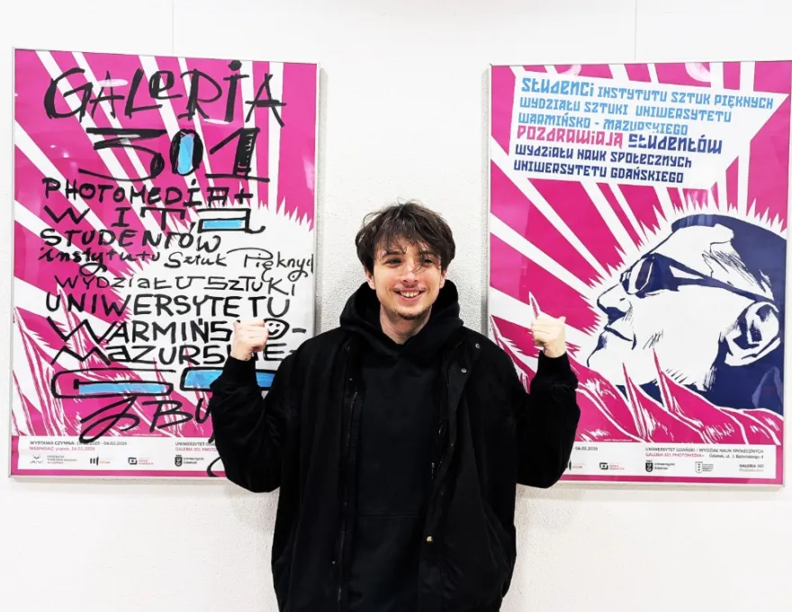 Chłopiec w czarnej bluzie na tle plakatu wystawy 