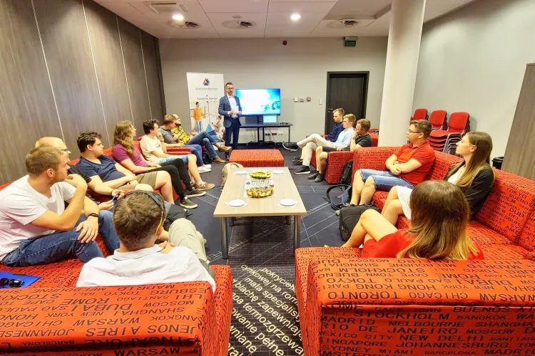 Spotkanie Akademii Biznesu - uczestnicy siedzą na kanapach, prof. Włodarczyk stoi przed nimi