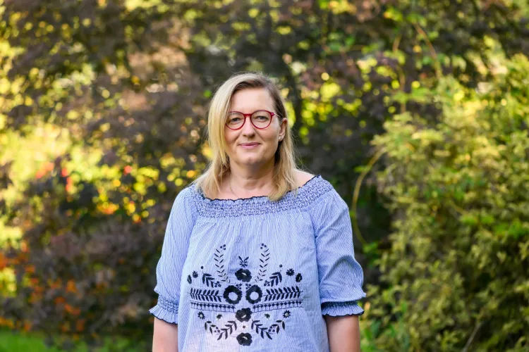 Agnieszka Jaszczak stoi wśród drzew w niebieskiej bluzce 