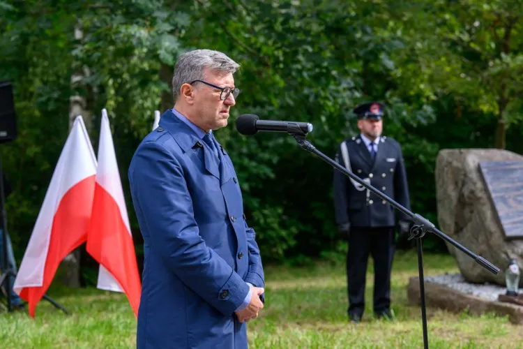 rektor UWM przemawia do mikrofonu, obok flaga Polski i głaz