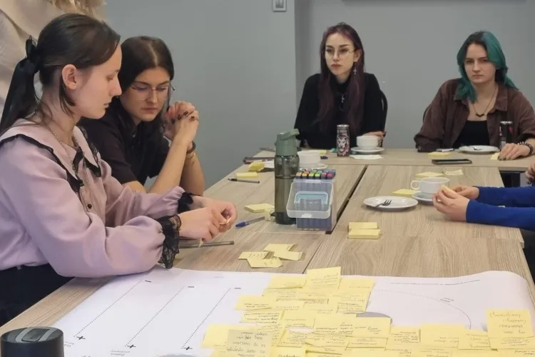 studentki siedzą przy stole, na którym są rozłożone różne kartki z pomysłami
