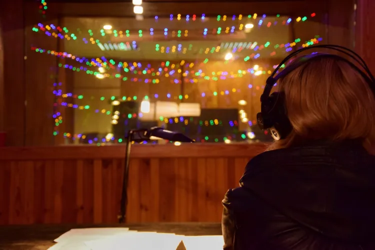 Studio radiowe, na pierwszym planie tyłem do obiektywu siedzi osoba w słuchawkach