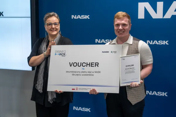 Marcin Merchel odbiera voucher od przedstawicielki organizatorów konkursu DISINFOHACK 2026