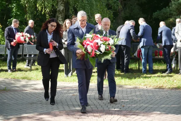 Troje przedstawicieli kolegium rektorskiego UWM niosą kwiaty i znicze