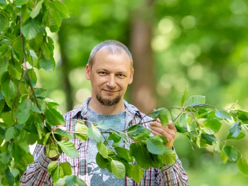 Marcin Michalak stoi przy drzewach i trzyma gałązkę 